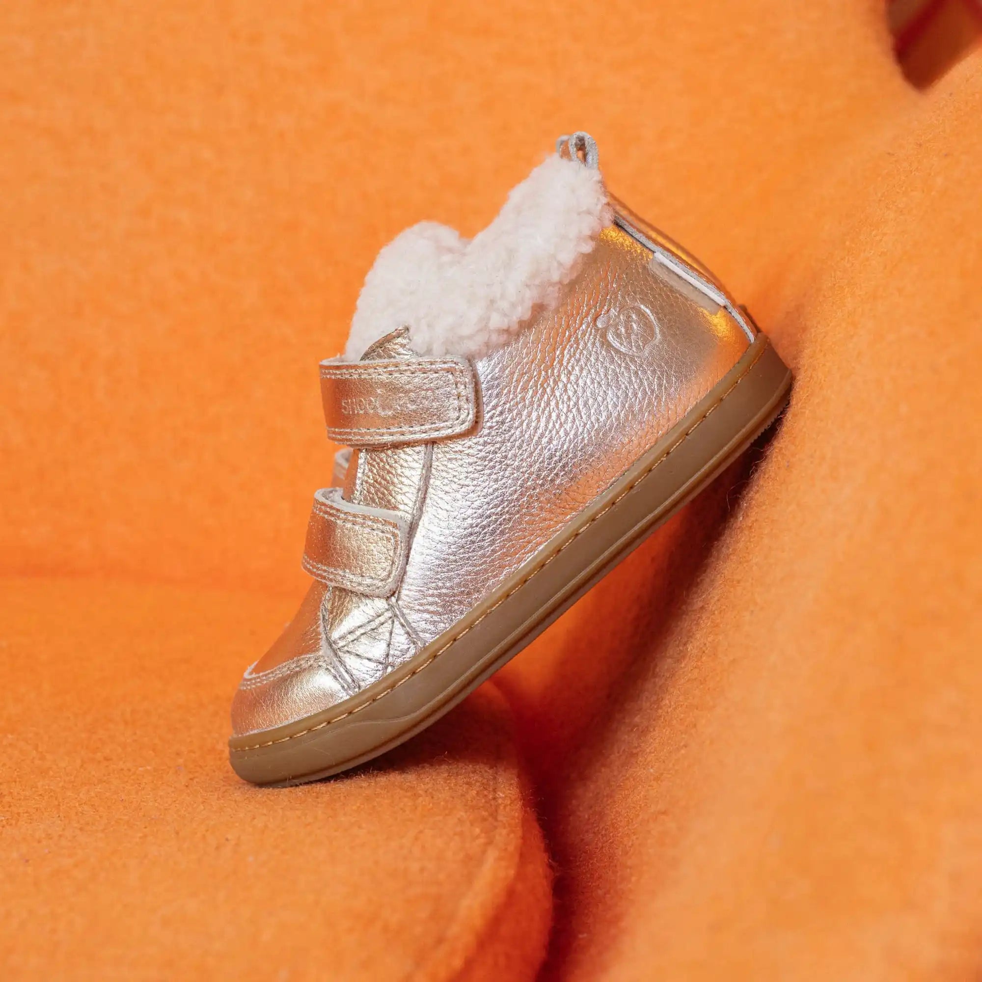 Chaussure montante en métal argenté avec intérieur en imitation de fourrure blanche et deux sangles en velcro.