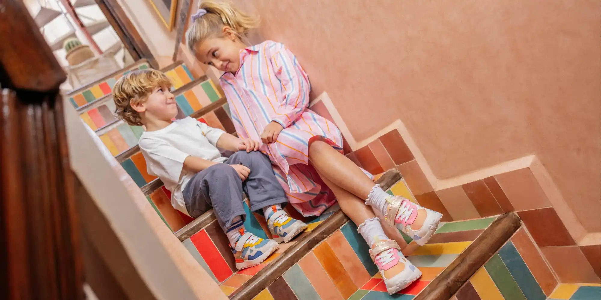 Deux enfants assis sur des escaliers colorés.