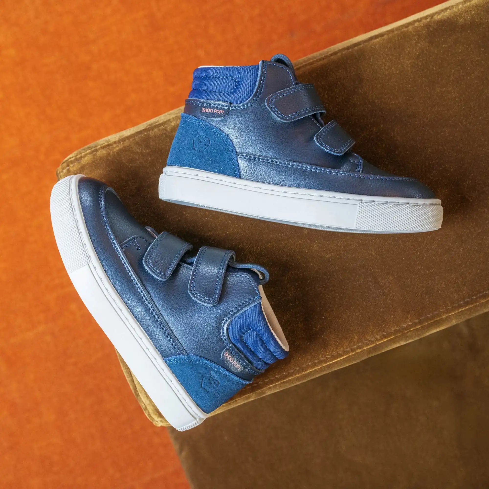 Deux paires de baskets montantes en cuir bleu avec des semelles blanches et trois bandes Velcro.