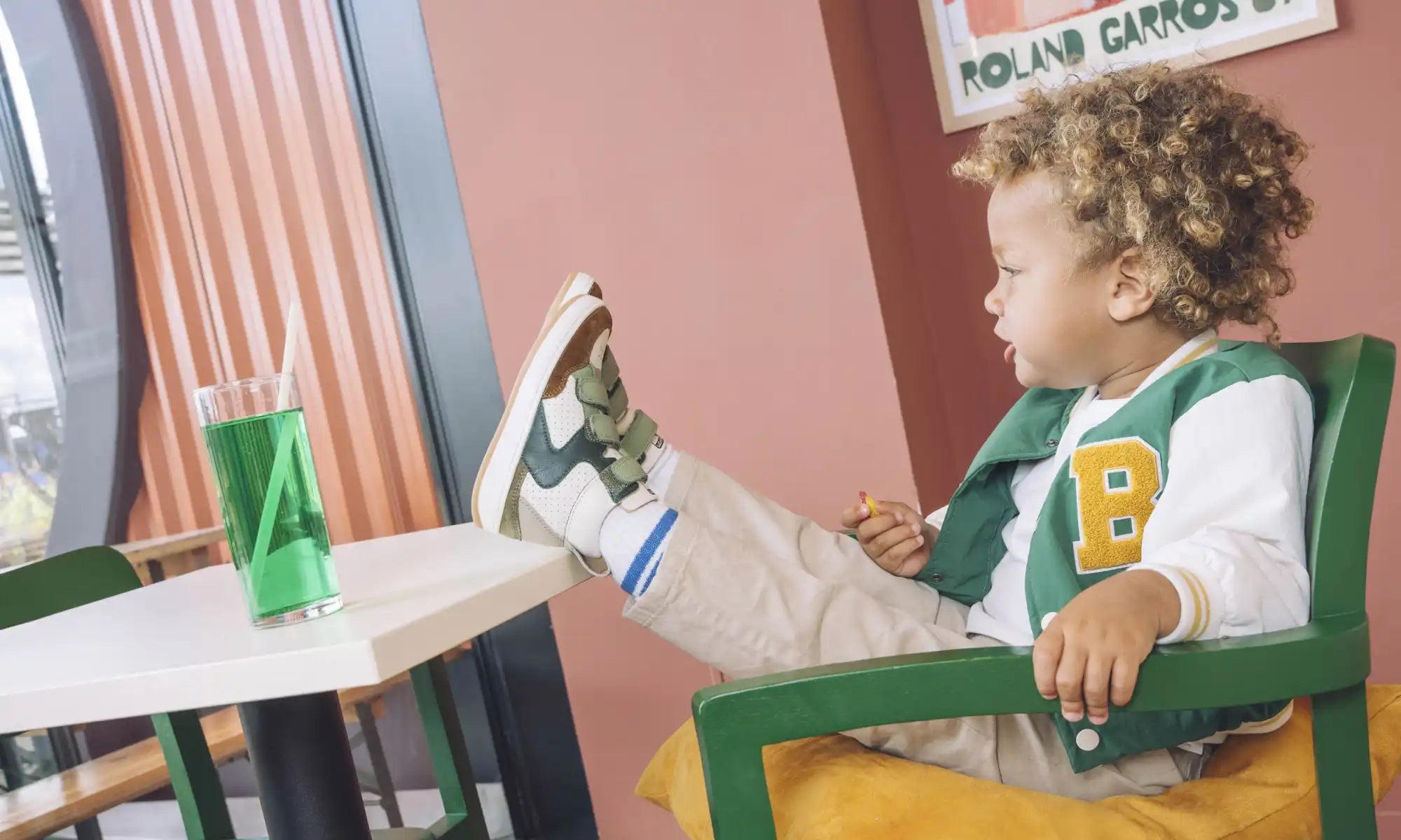 Un jeune enfant portant une veste de style universitaire est assis dans une chaise jaune.